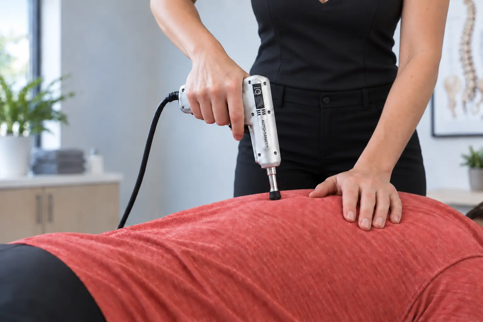 Female chiropractor using an Impulse iQ instrument on a clothed patient’s upper back